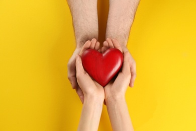 Couple holding decorative heart on color background, top view