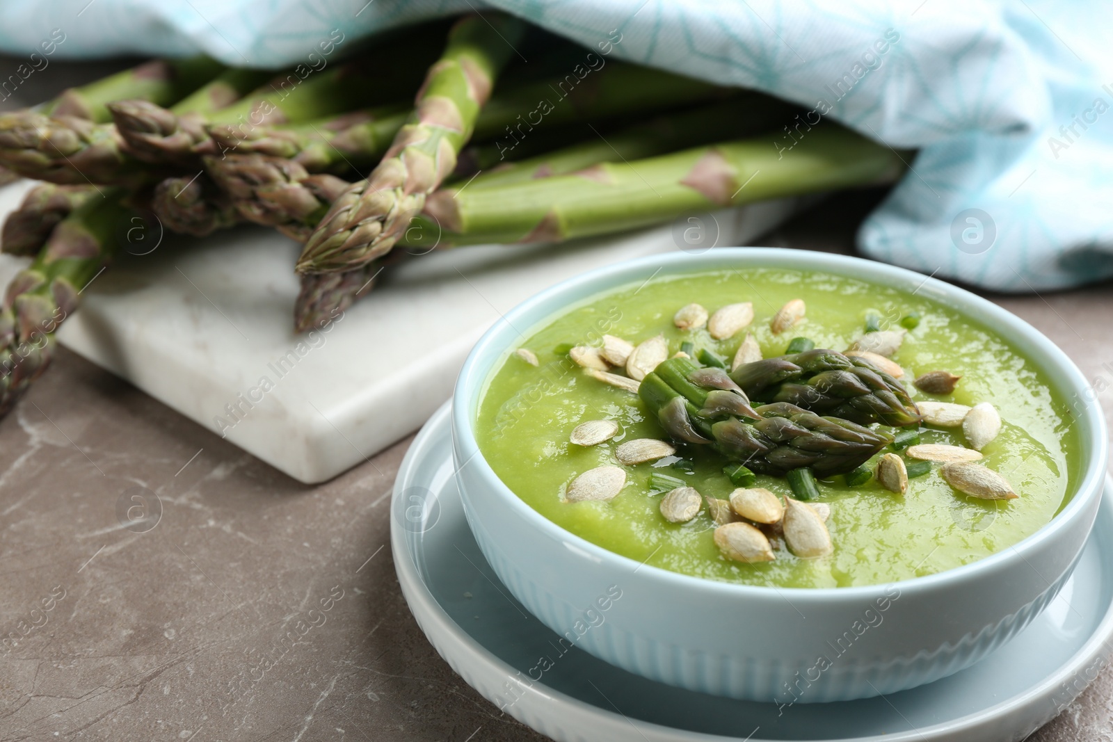 Photo of Delicious asparagus soup in bowl on grey marble table