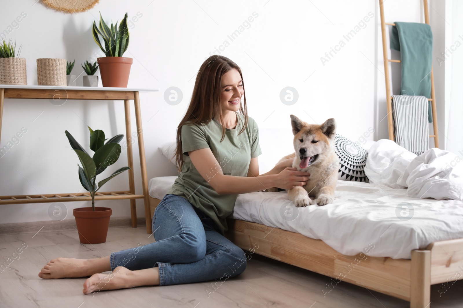 Photo of Young woman and Akita Inu dog in bedroom decorated with houseplants