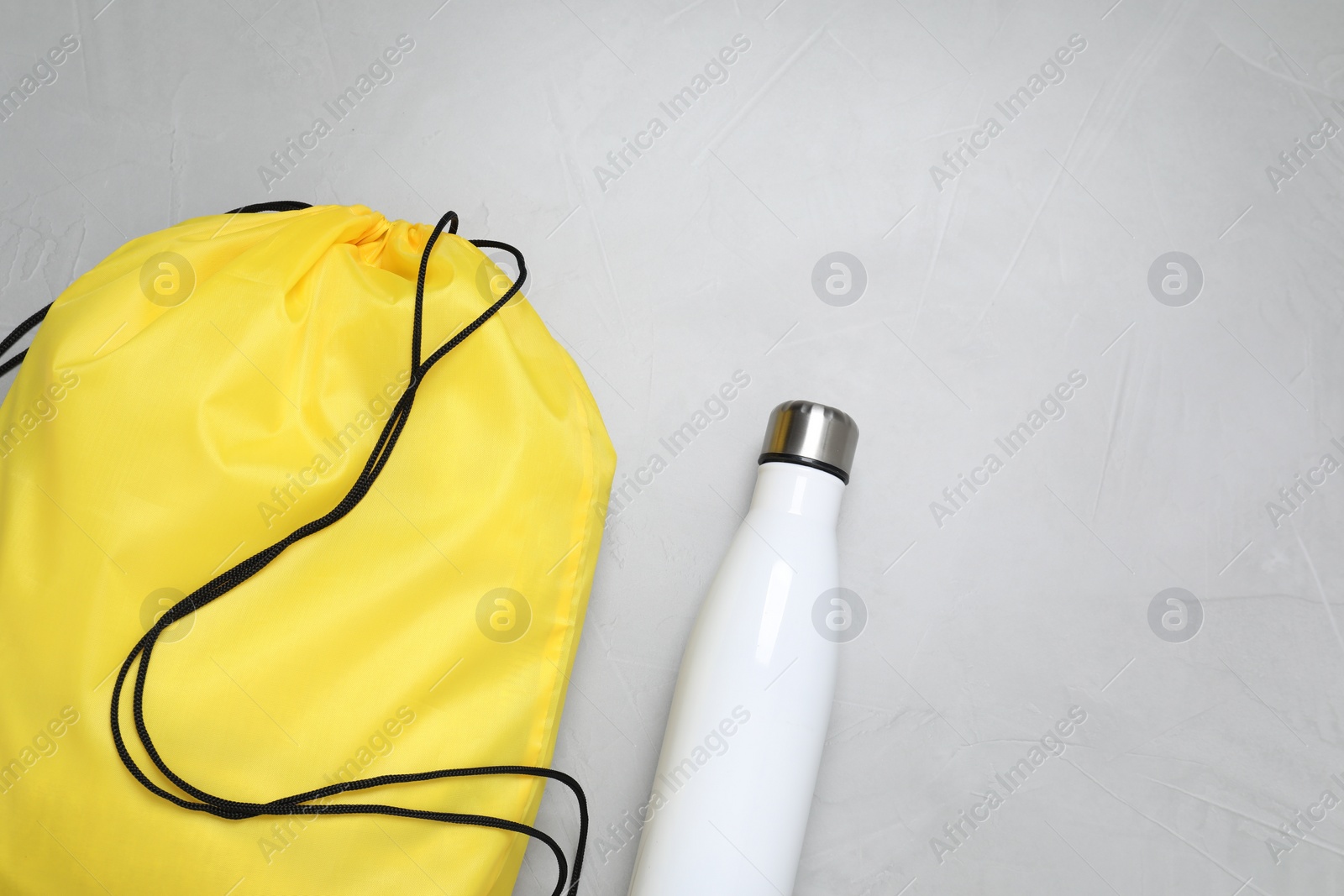 Photo of Yellow drawstring bag and thermo bottle on light background, flat lay. Space for text