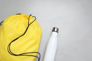 Photo of Yellow drawstring bag and thermo bottle on light background, flat lay. Space for text