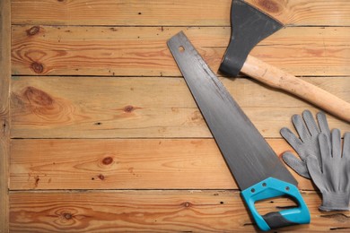 Photo of Saw with light blue handle, axe and gloves on wooden background, flat lay. Space for text