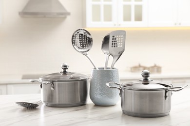 Photo of Stainless steel pots and kitchen utensils on white table indoors