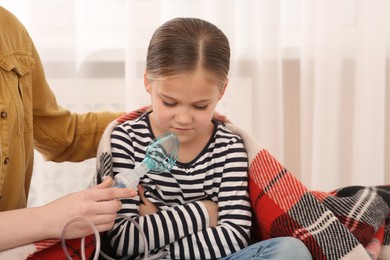 Photo of Mother helping her sick daughter with nebulizer inhalation at home