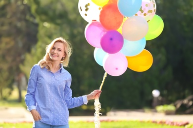 Young woman with colorful balloons in park on sunny day