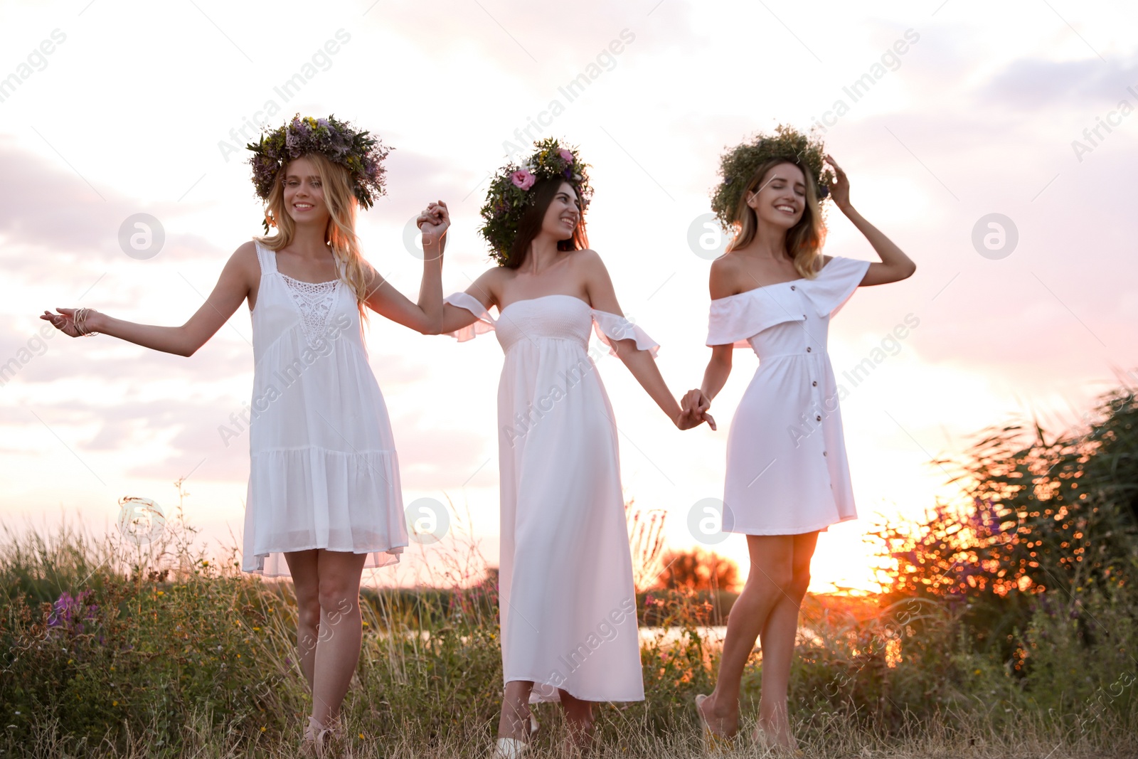 Photo of Young women wearing wreaths made of beautiful flowers outdoors at sunset