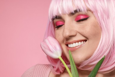 Photo of Smiling woman with bright makeup, fake freckles and tulip on pink background, closeup. Space for text
