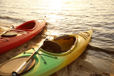 Photo of Colorful kayaks with paddles near water on river beach at sunset. Summer camp activity
