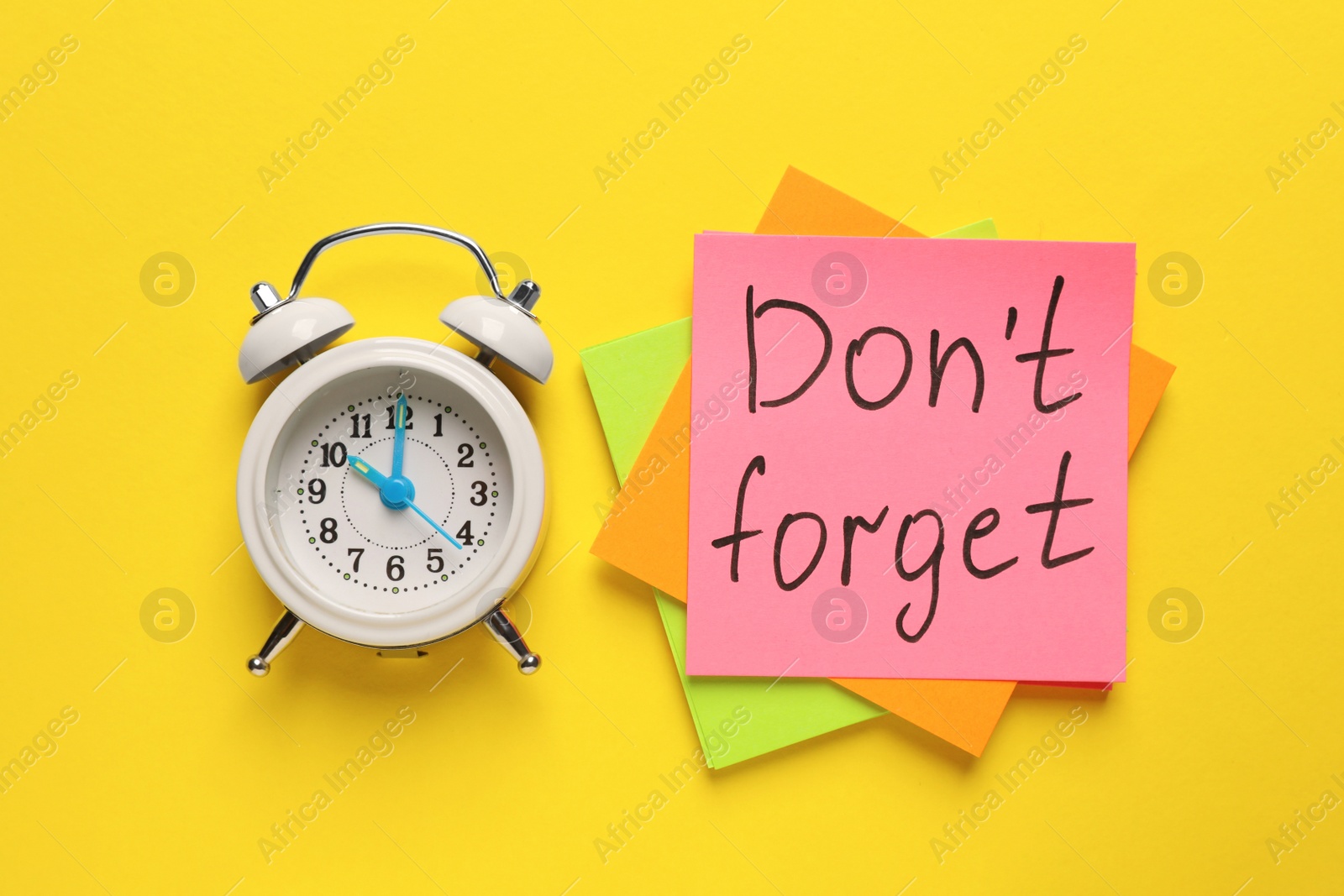 Photo of Alarm clock and reminder notes with phrase Don't forget on yellow background, flat lay