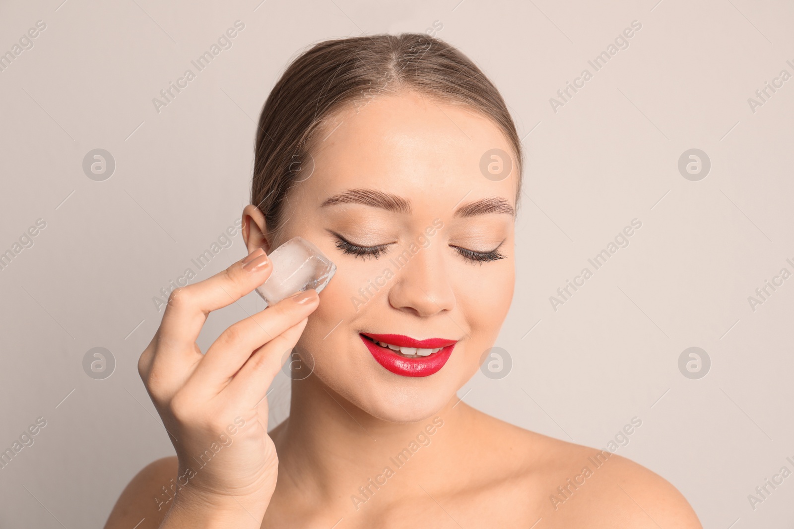 Photo of Young woman with ice cube on light background. Skin care