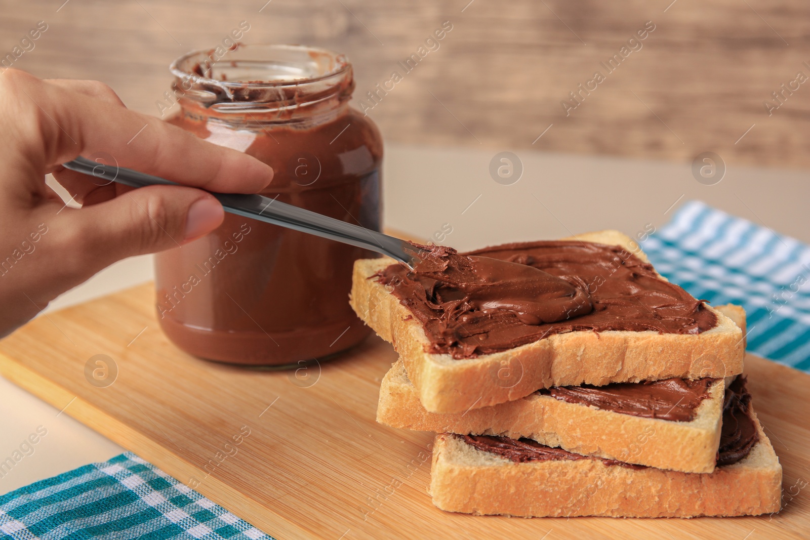 Photo of Woman spreading chocolate paste onto bread at table, closeup