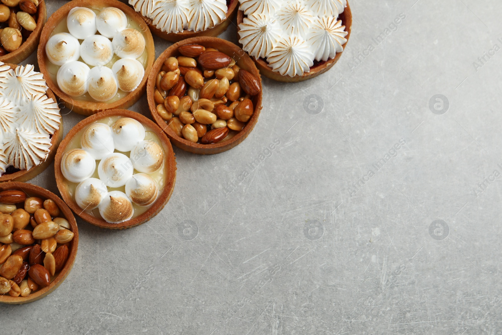 Photo of Many different tartlets on grey table, flat lay with space for text. Delicious dessert