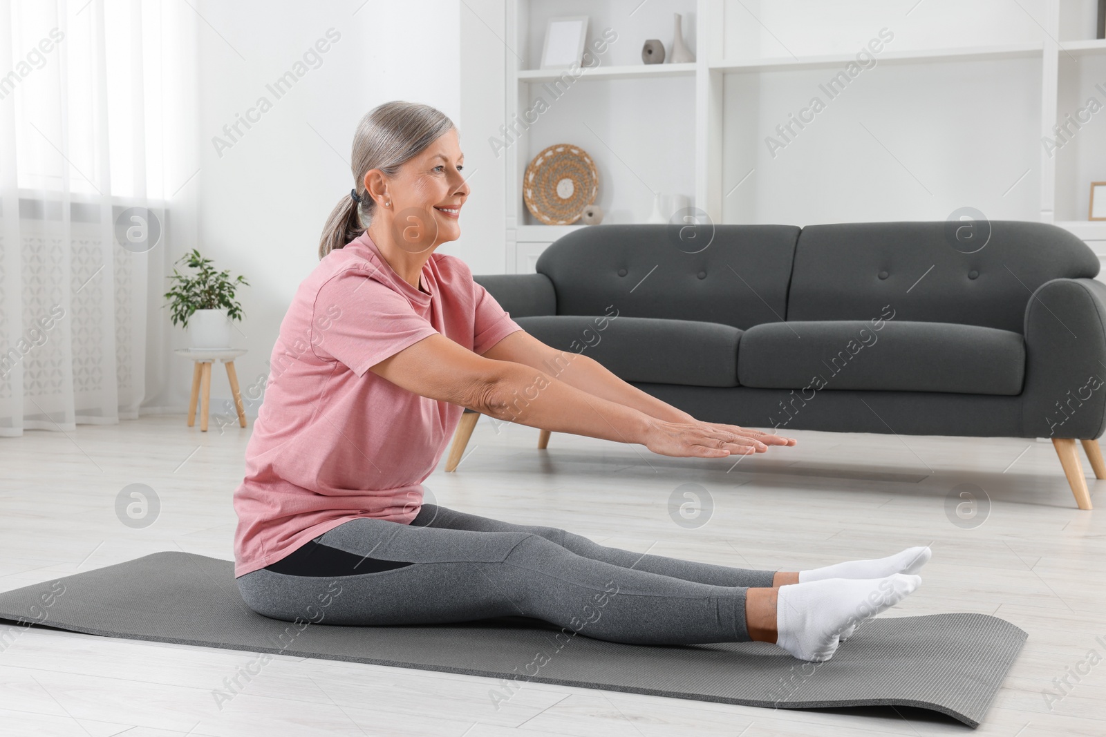 Photo of Senior woman in sportswear stretching on fitness mat at home