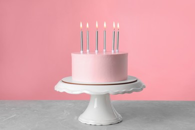 Photo of Birthday cake with burning candles on table against pink background