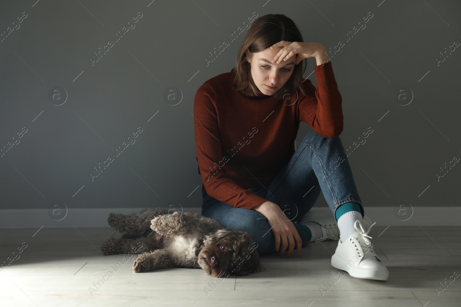 Photo of Sad young woman sitting on floor near grey wall indoors