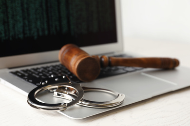 Photo of Laptop, wooden gavel and handcuffs on white table, closeup. Cyber crime