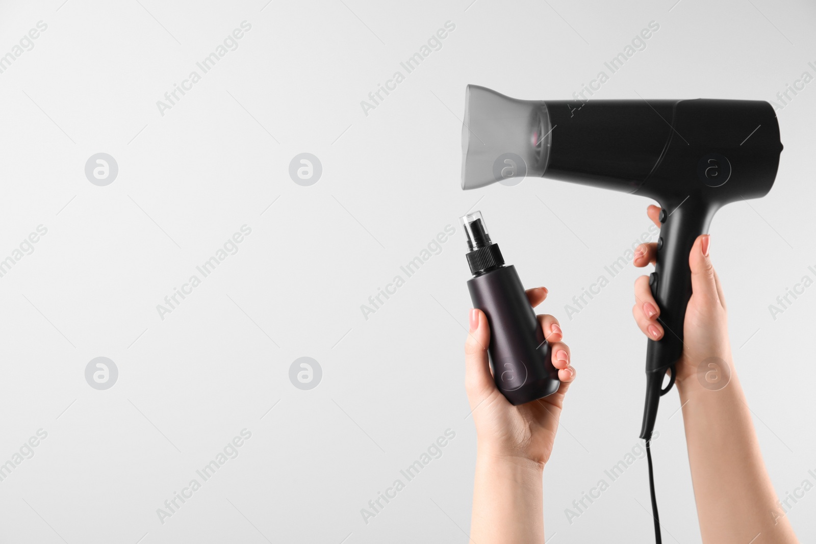 Photo of Woman holding spray bottle with thermal protection and hairdryer on white background, closeup. Space for text