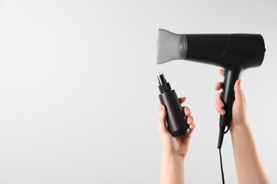 Photo of Woman holding spray bottle with thermal protection and hairdryer on white background, closeup. Space for text