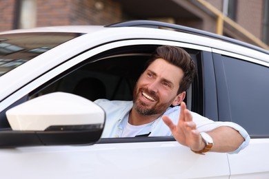 Photo of Happy bearded man looking out of car window on city street, view from outside. Enjoying trip