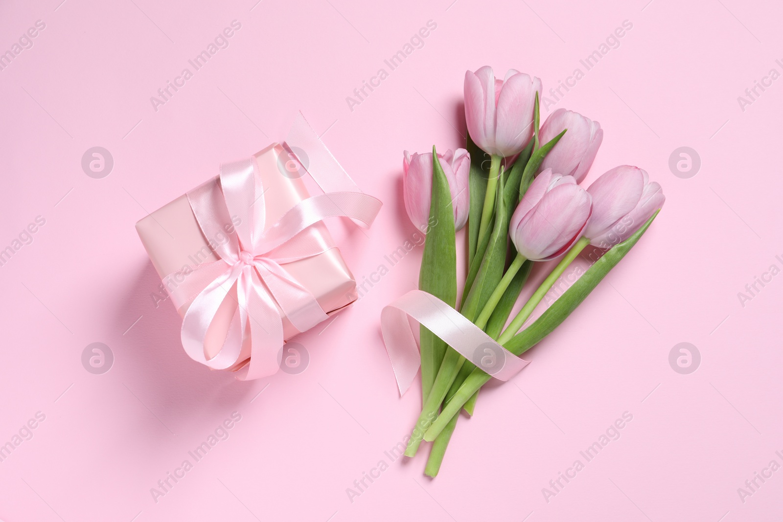 Photo of Beautiful gift box with bow and tulips on pink background, flat lay