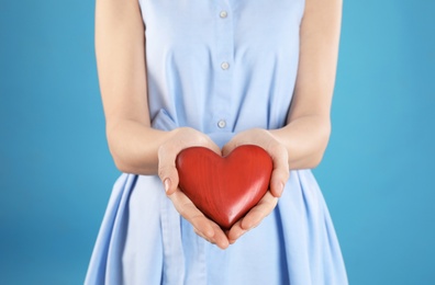 Woman holding decorative heart on color background, closeup