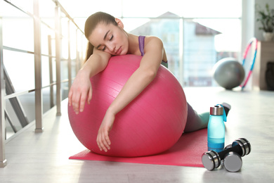 Photo of Lazy young woman with sport equipment sleeping on yoga mat indoors