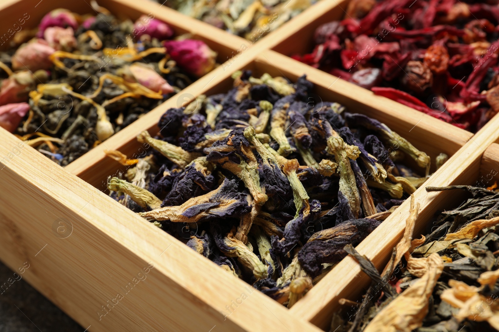 Photo of Different dry herbal teas in wooden box, closeup