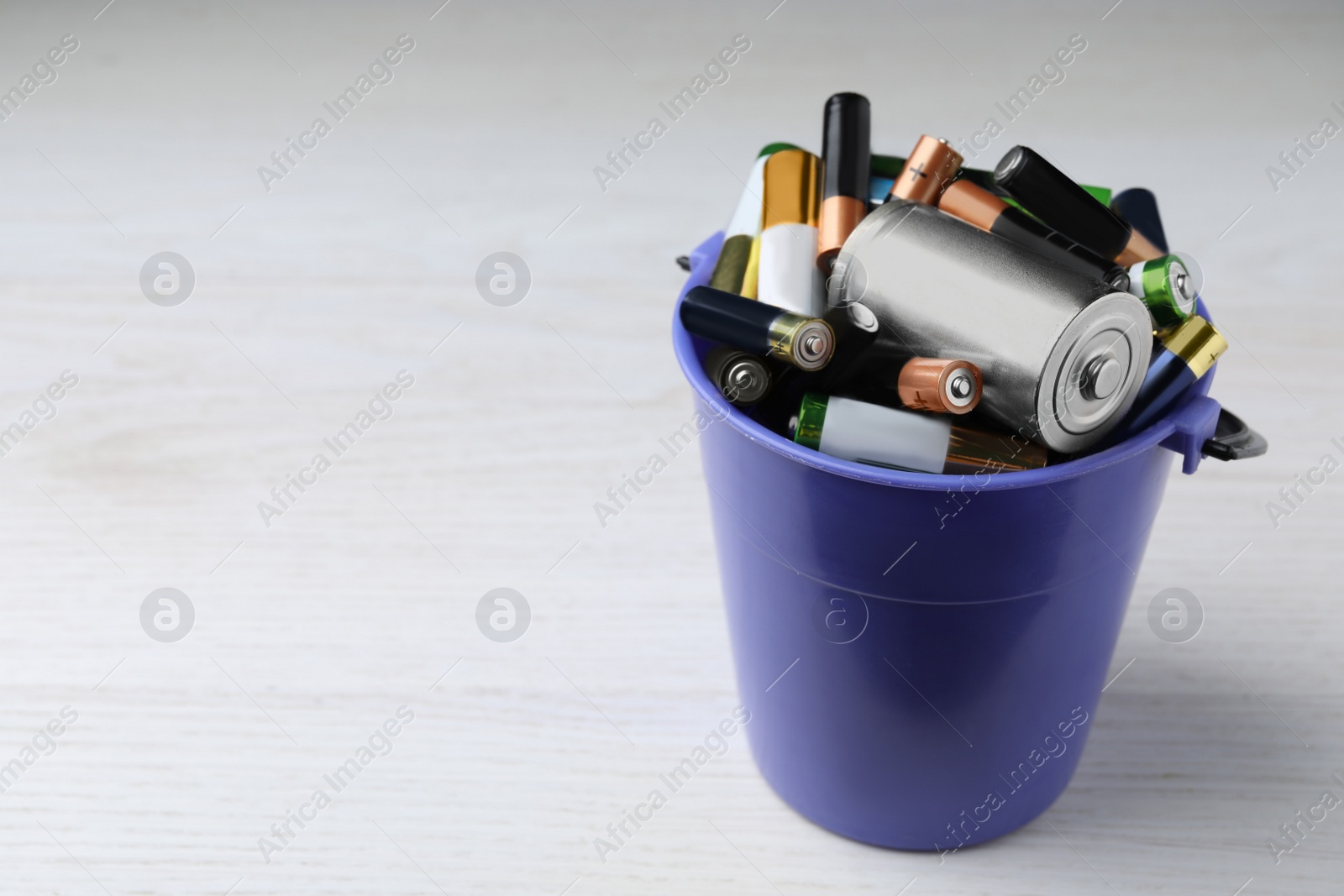 Image of Used batteries in bucket on white table, space for text