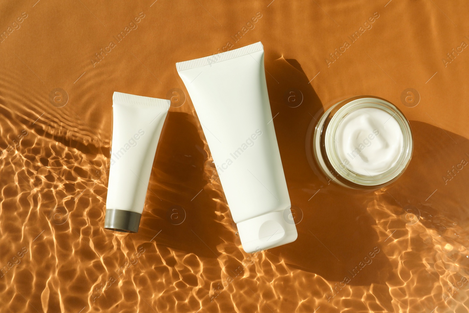 Photo of Tubes and jar with moisturizing cream in water on orange background, top view