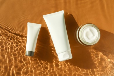 Tubes and jar with moisturizing cream in water on orange background, top view