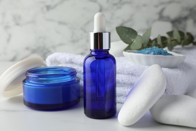 Spa composition. Cosmetic products, sea salt, towel, stones and eucalyptus branch on white marble table, closeup