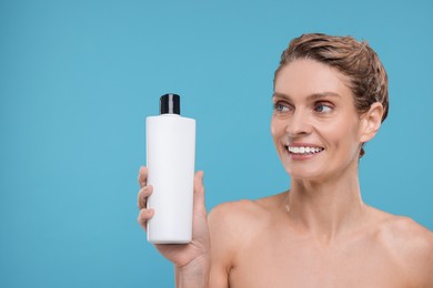 Washing hair. Portrait of beautiful happy woman with bottle on light blue background, space for text