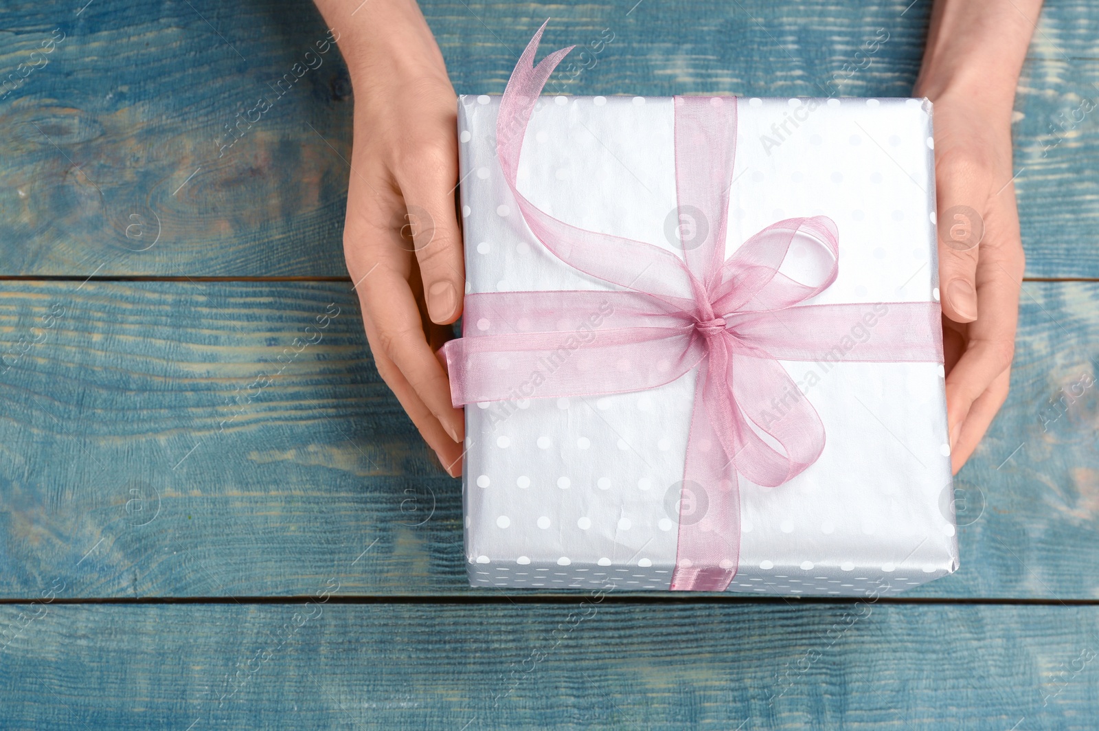 Photo of Young woman holding beautiful gift box on wooden background, top view