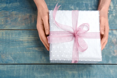 Young woman holding beautiful gift box on wooden background, top view