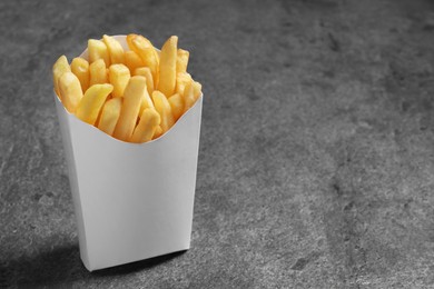 Photo of Delicious french fries in paper box on grey table, space for text
