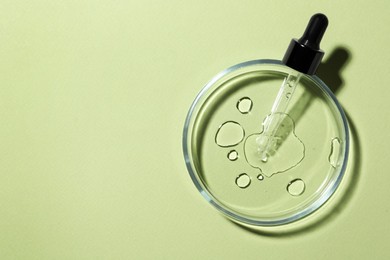 Photo of Petri dish with sample and pipette on light green background, top view. Space for text