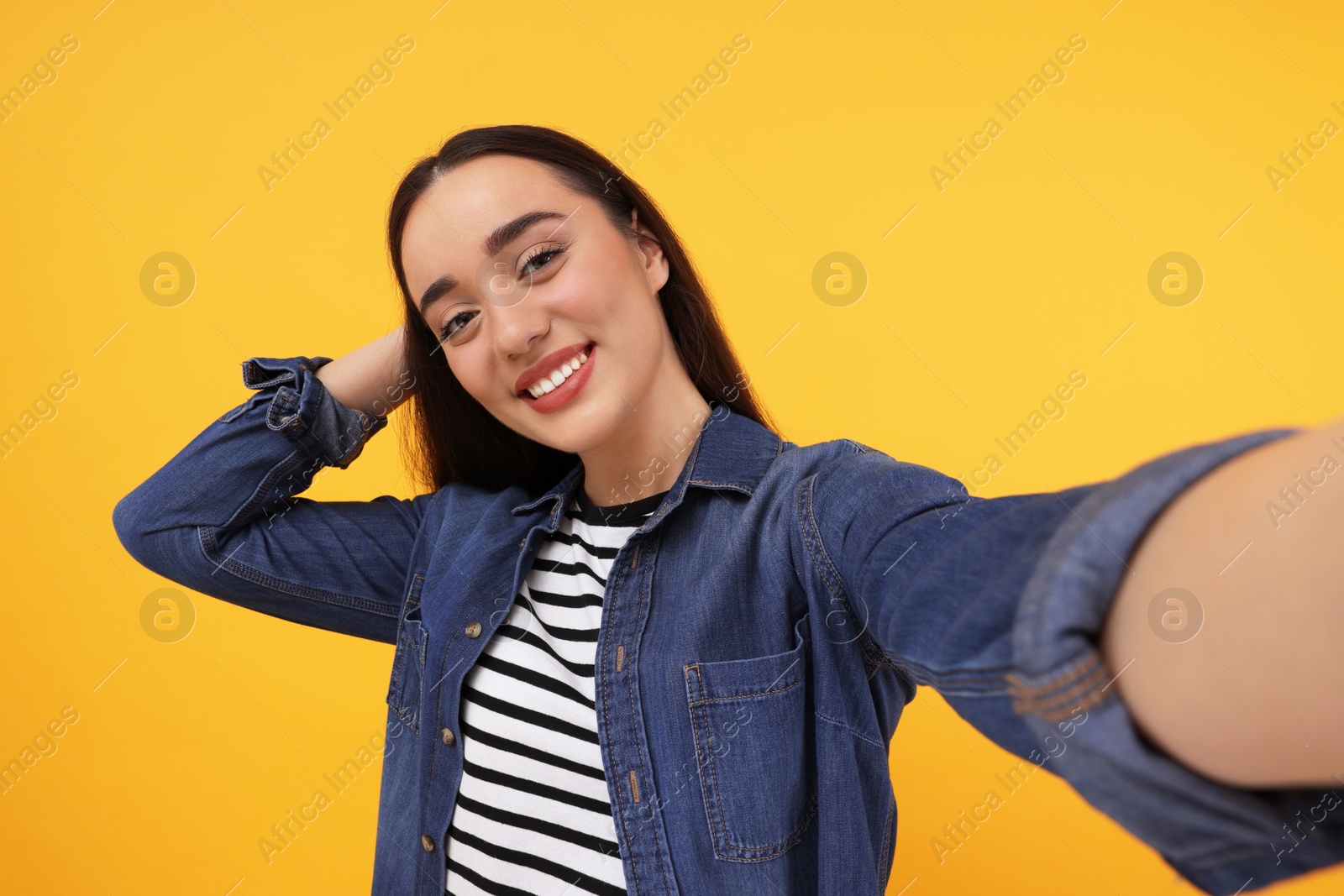 Photo of Smiling young woman taking selfie on yellow background