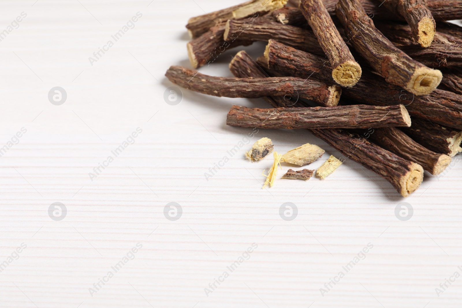 Photo of Dried sticks of liquorice root on white wooden table, space for text