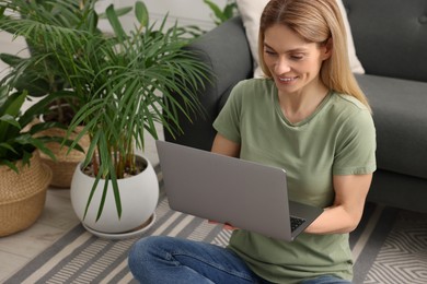 Woman using laptop on floor in room with beautiful potted houseplants