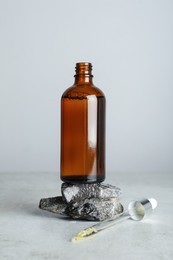 Photo of Bottle of hydrophilic oil, rocks and pipette on white table