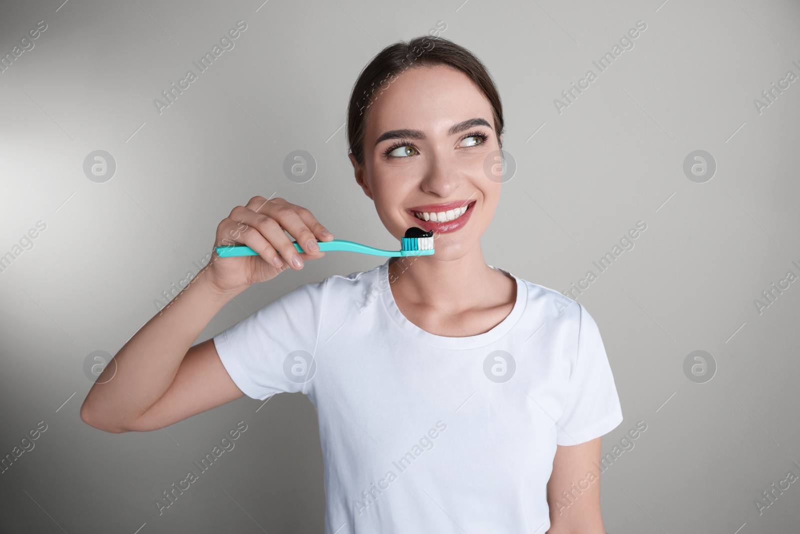 Photo of Young woman holding toothbrush with charcoal toothpaste on grey background