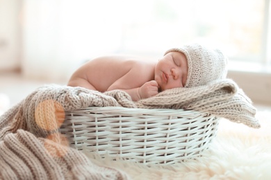 Adorable newborn baby lying in basket with knitted plaid indoors