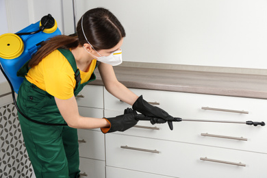 Pest control worker in protective mask spraying pesticide indoors