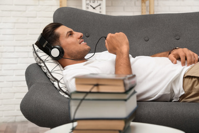 Photo of Man with headphones connected to book
on sofa indoors. Audiobook concept