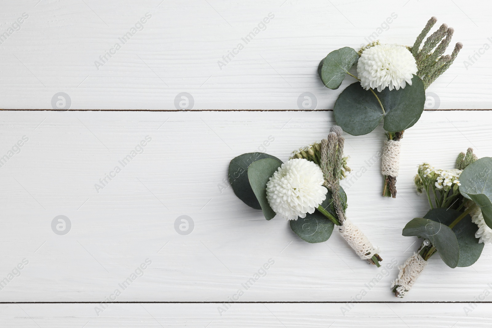 Photo of Small stylish boutonnieres on white wooden table, flat lay. Space for text