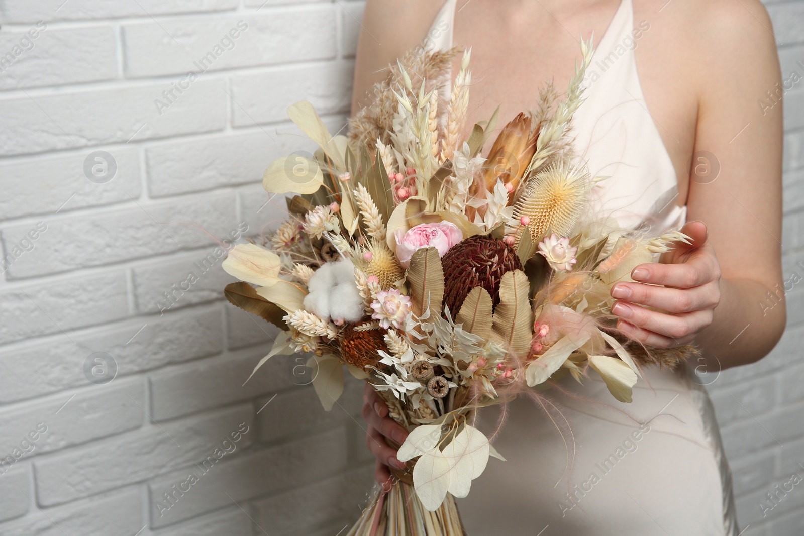 Photo of Bride holding beautiful dried flower bouquet near white brick wall, closeup