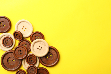 Many colorful sewing buttons on yellow background, flat lay. Space for text