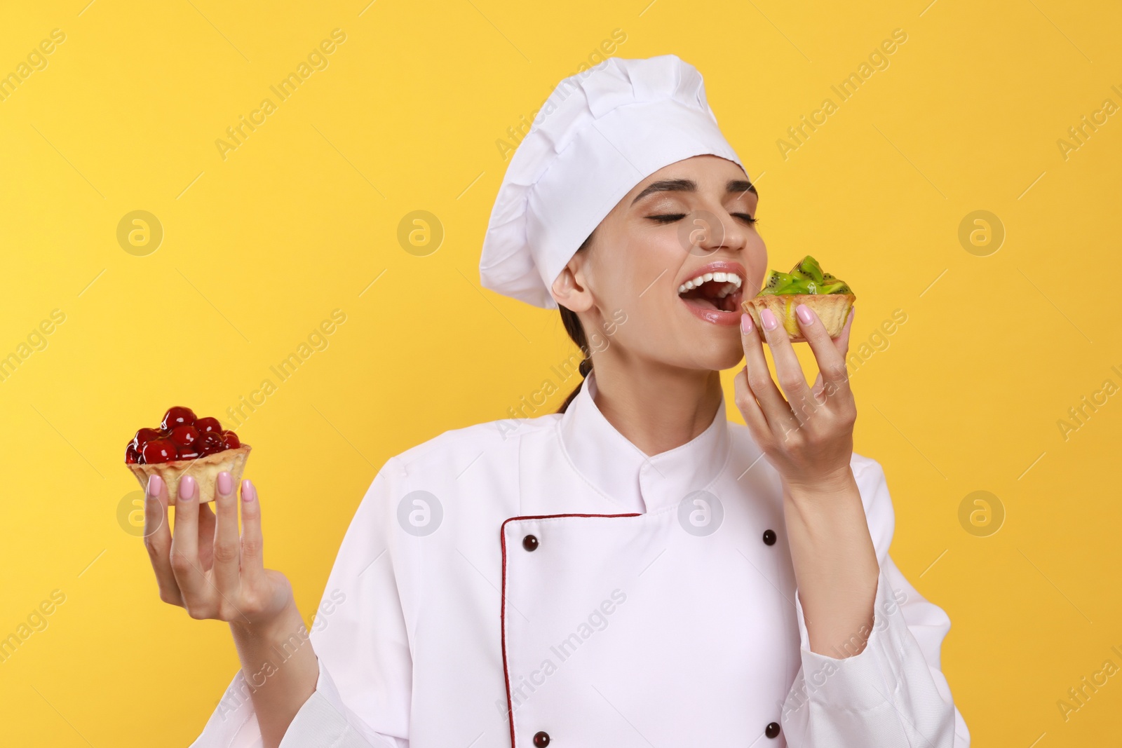 Photo of Professional confectioner in uniform with delicious tartlets on yellow background