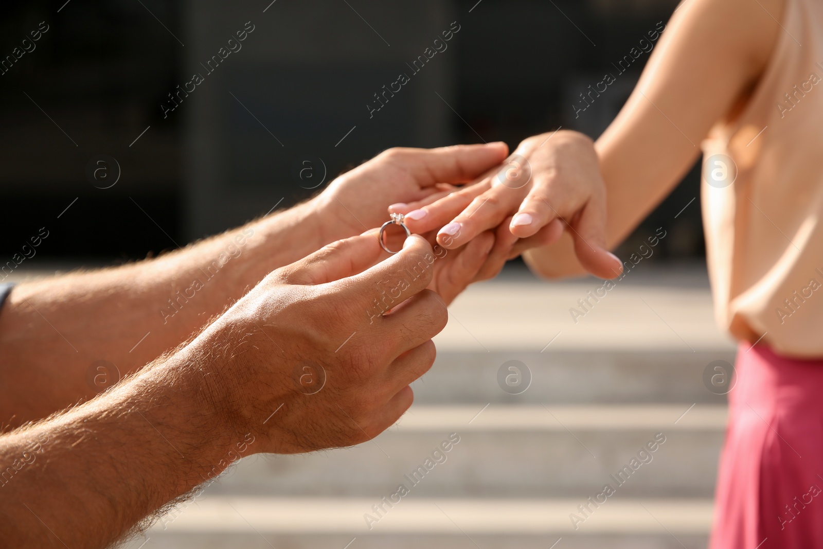 Photo of Man putting engagement ring on his girlfriend's finger outdoors, closeup