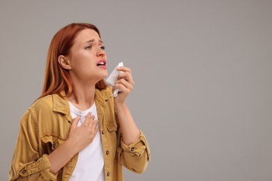Suffering from allergy. Young woman with tissue sneezing on grey background, space for text